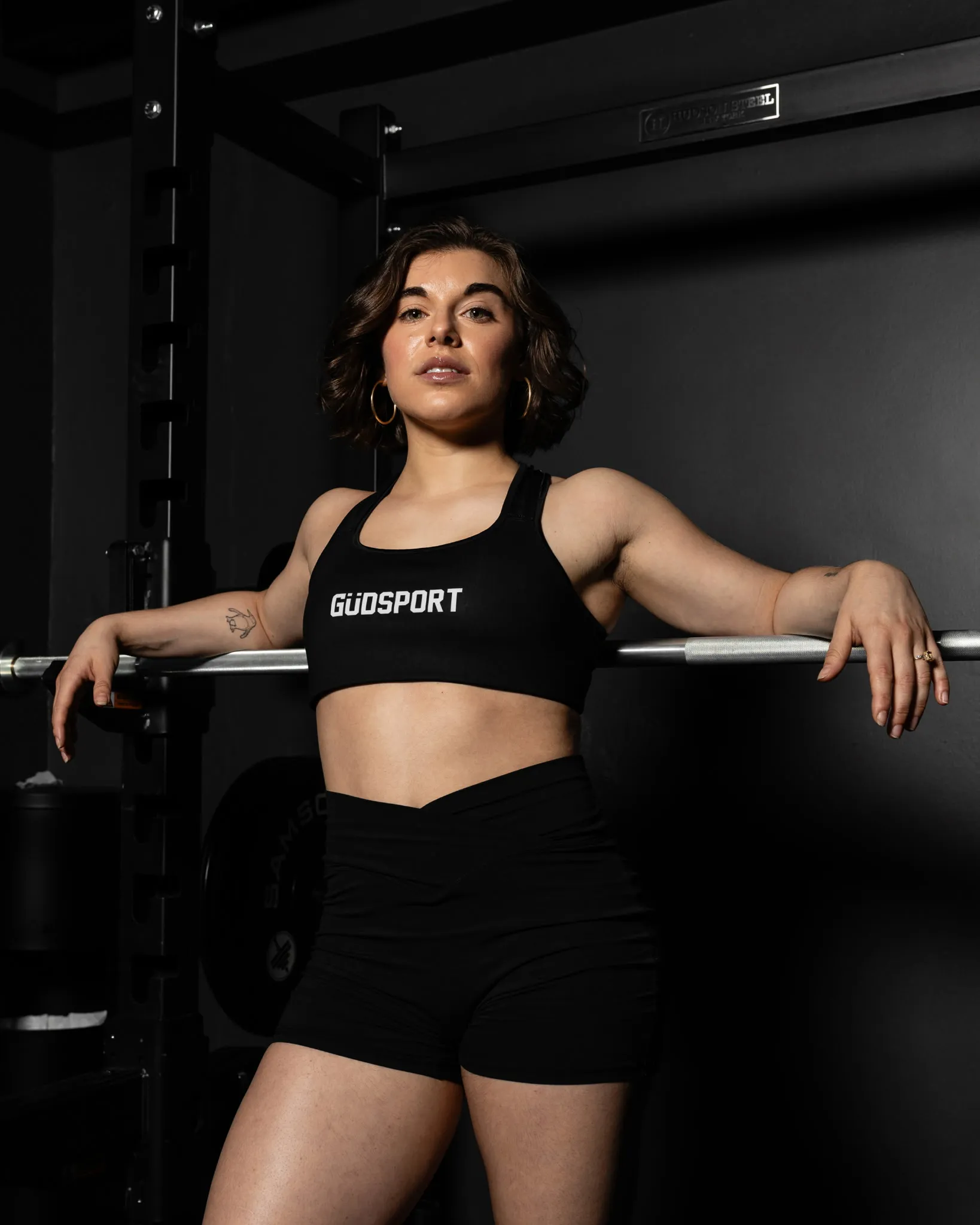 Coach Juliana leaning on a barbell in a squat rack